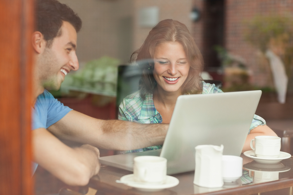 Two laughing students looking at laptop in college canteen